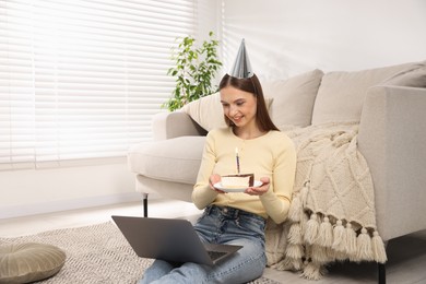 Photo of Birthday celebration. Happy woman with piece of cake having video call via laptop at home