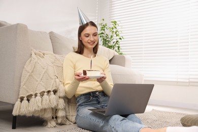 Photo of Birthday celebration. Happy woman with piece of cake having video call via laptop at home