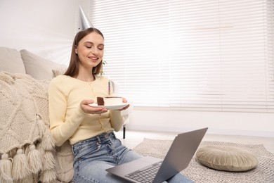 Photo of Birthday celebration. Happy woman with piece of cake having video call via laptop at home