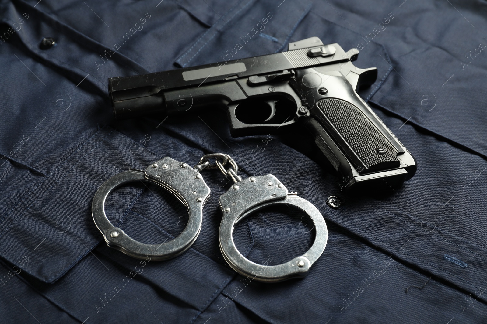 Black gun and handcuffs on dark blue uniform, above view. Police equipment Photo of Black gun and handcuffs on dark blue uniform, above view. Police equipment