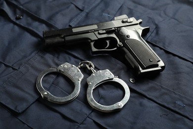 Photo of Black gun and handcuffs on dark blue uniform, above view. Police equipment