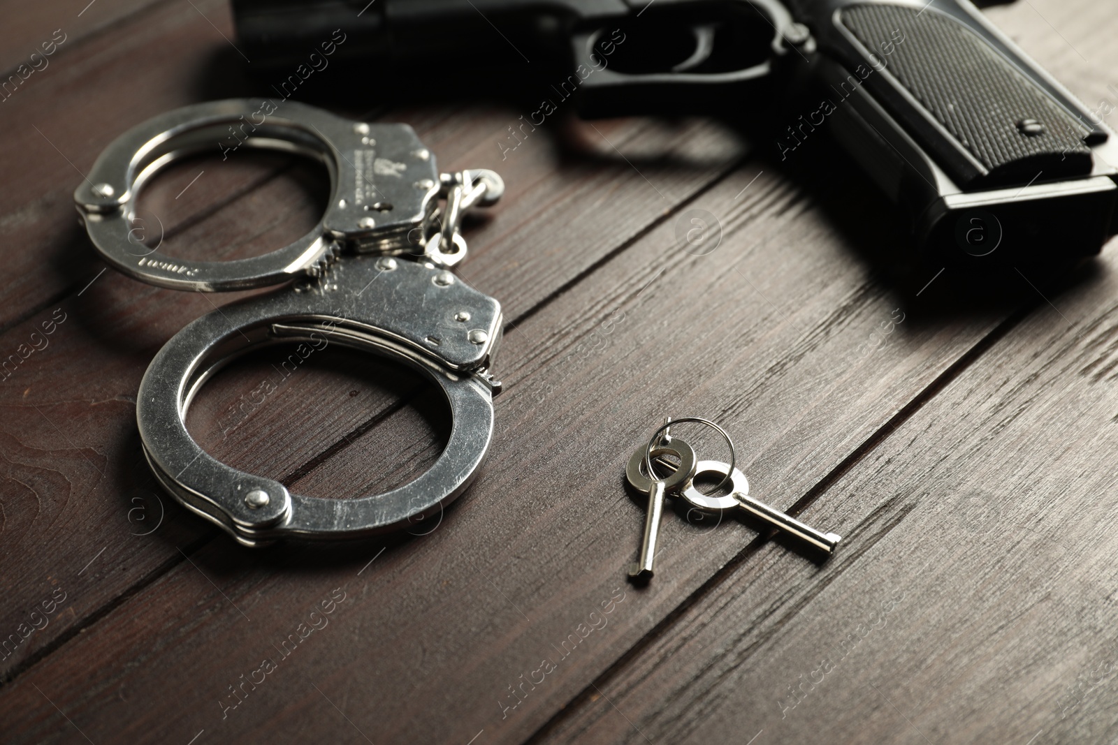 Handcuffs, keys and gun on wooden table, closeup. Police equipment Photo of Handcuffs, keys and gun on wooden table, closeup. Police equipment