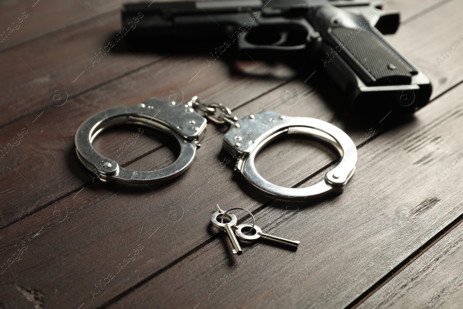 Photo of Handcuffs, keys and gun on wooden table, closeup. Police equipment