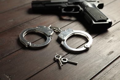 Photo of Handcuffs, keys and gun on wooden table, closeup. Police equipment
