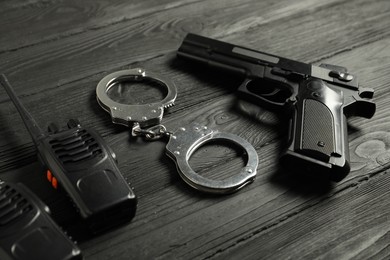 Photo of Gun, handcuffs and walkie talkies on black wooden table, closeup. Police equipment