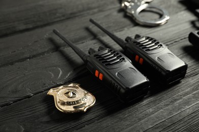 Photo of Walkie talkies, badge and handcuffs on black wooden table, closeup. Police equipment