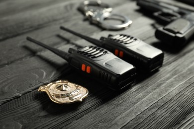 Photo of Walkie talkies, badge, gun and handcuffs on black wooden table, closeup. Police equipment