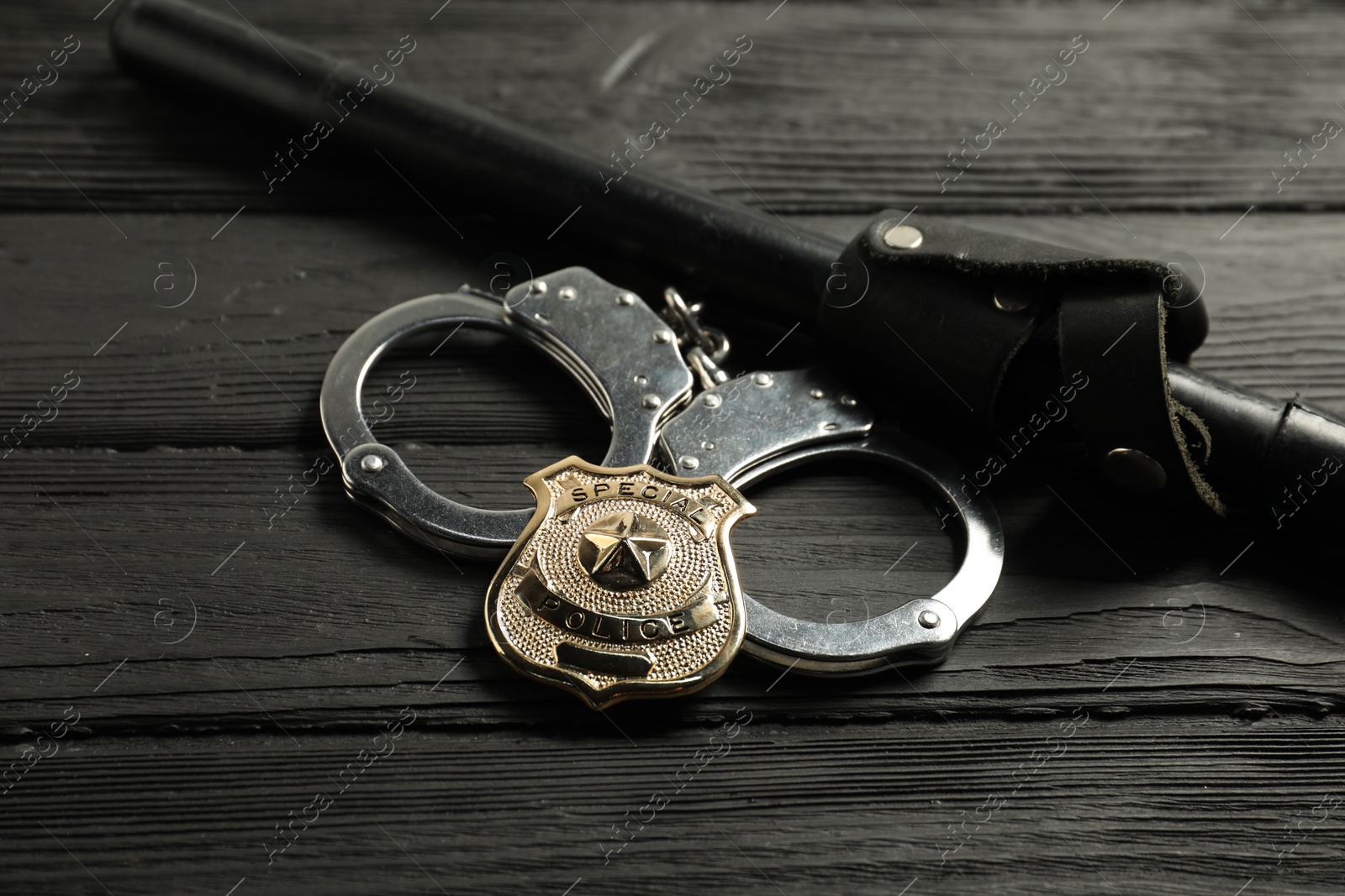 Police badge, handcuffs and baton on black wooden table, closeup Photo of Police badge, handcuffs and baton on black wooden table, closeup