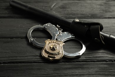 Photo of Police badge, handcuffs and baton on black wooden table, closeup