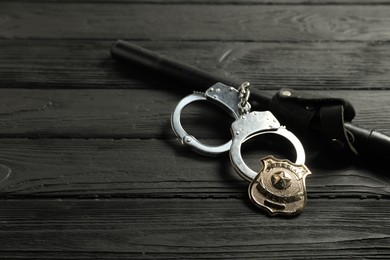 Photo of Police badge, handcuffs and baton on black wooden table, closeup. Space for text