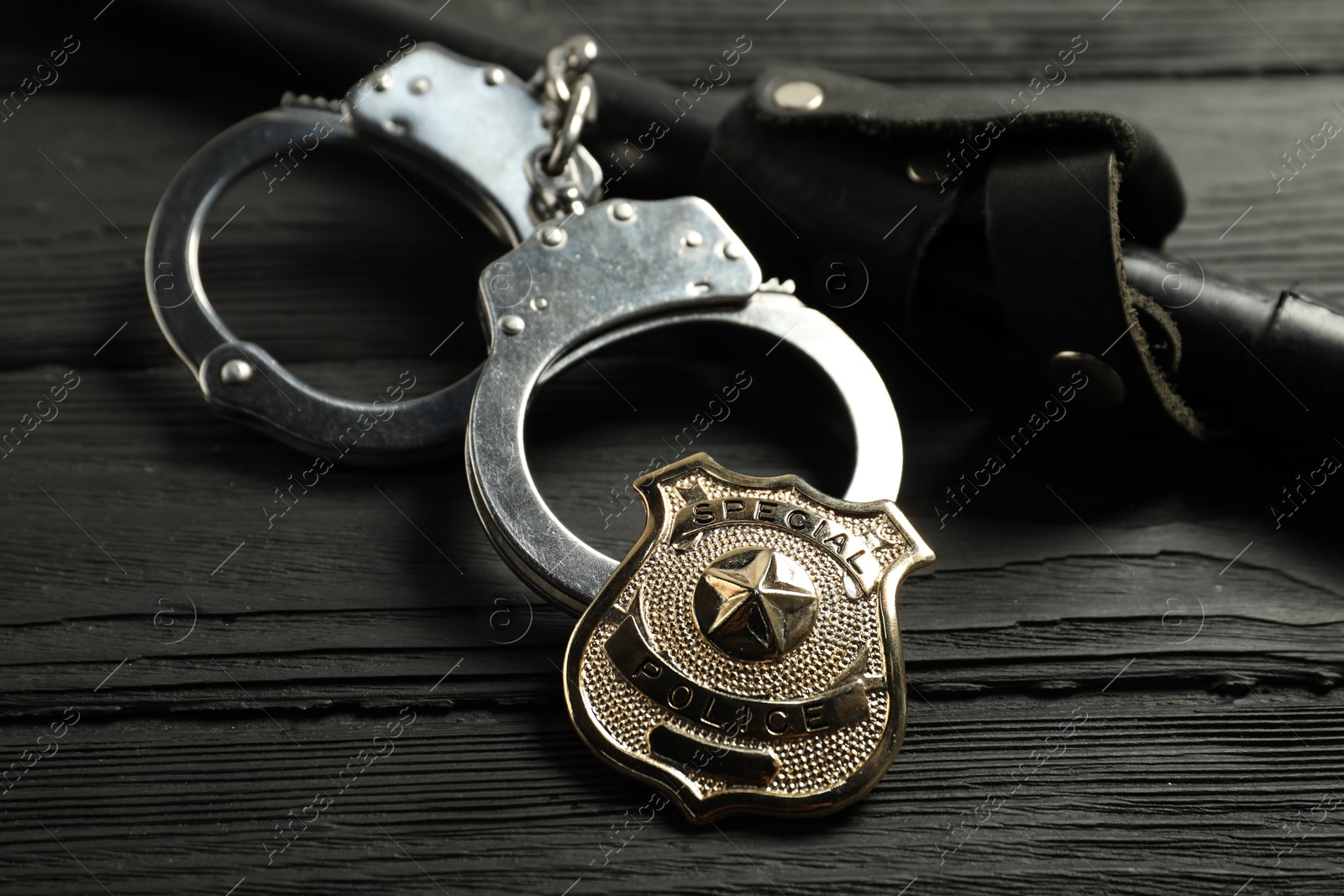 Police badge, handcuffs and baton on black wooden table, closeup Photo of Police badge, handcuffs and baton on black wooden table, closeup
