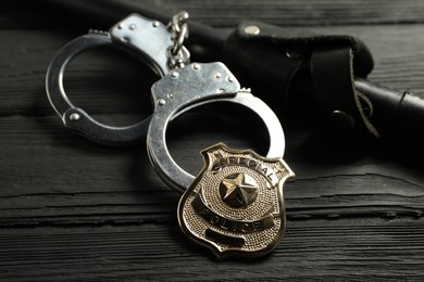 Photo of Police badge, handcuffs and baton on black wooden table, closeup