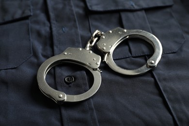 Photo of Handcuffs on dark blue uniform, closeup. Police equipment