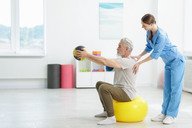 Photo of Doctor and patient exercising with medicine ball in clinic, space for text