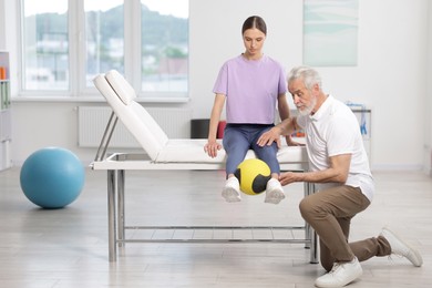 Photo of Doctor and patient exercising with medicine ball in clinic