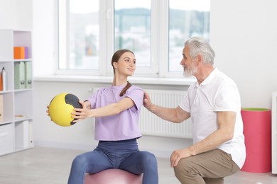 Photo of Doctor and patient exercising with medicine ball in clinic