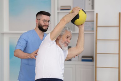 Photo of Doctor and patient exercising with medicine ball in clinic