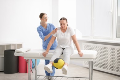Photo of Doctor and patient exercising with medicine ball in clinic