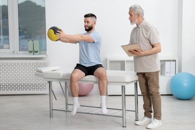 Photo of Doctor and patient exercising with medicine ball in clinic