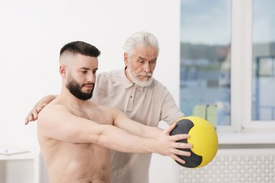 Photo of Doctor and patient exercising with medicine ball in clinic