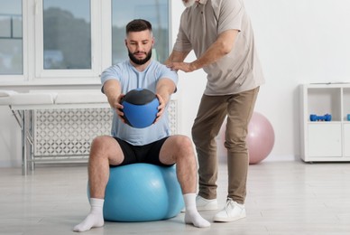 Photo of Doctor and patient exercising with medicine ball in clinic, space for text
