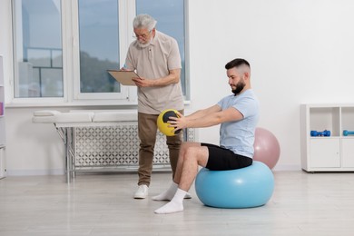 Photo of Doctor and patient exercising with medicine ball in clinic