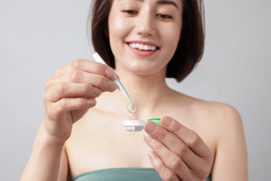 Photo of Woman taking contact lens out of case on light background, selective focus