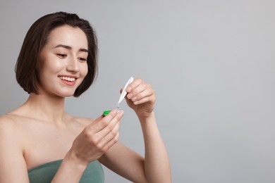 Photo of Woman taking contact lens out of case on light background. Space for text