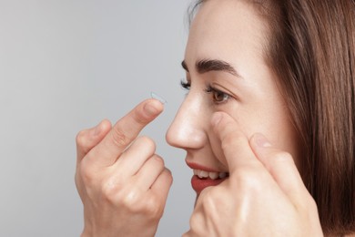 Photo of Woman putting in contact lens on light background, closeup