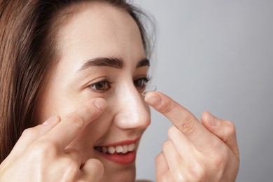 Photo of Woman putting in contact lens on light background, closeup