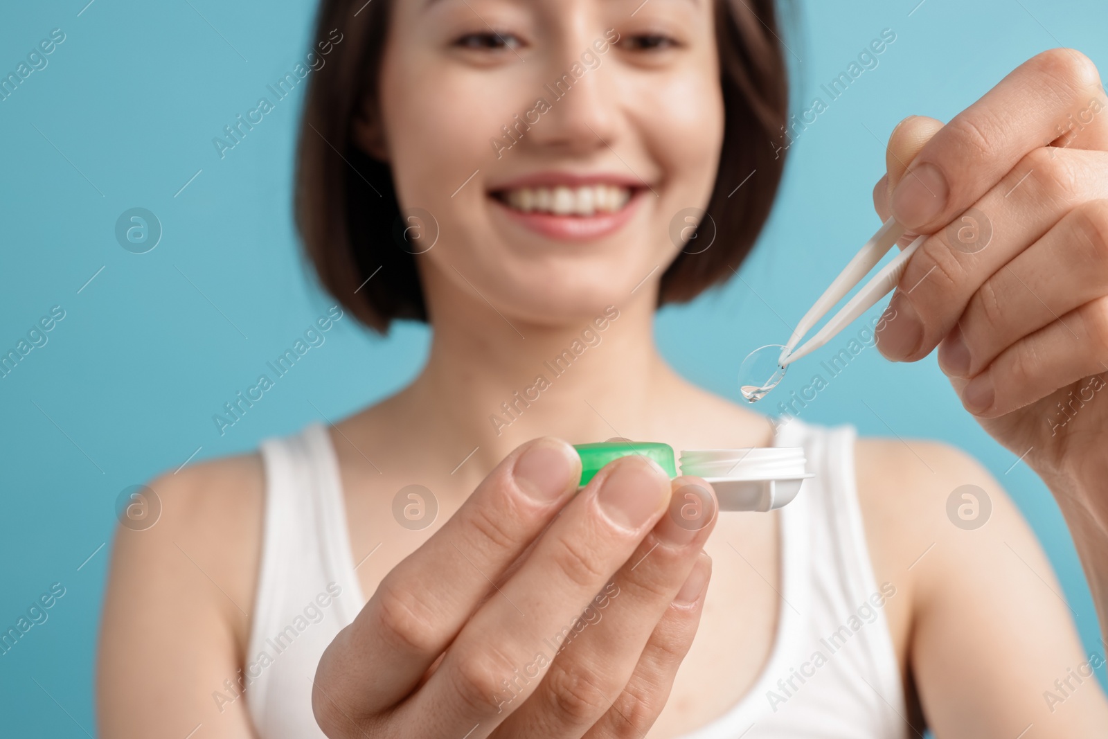 Woman taking contact lens out of case on light blue background, selective focus Photo of Woman taking contact lens out of case on light blue background, selective focus