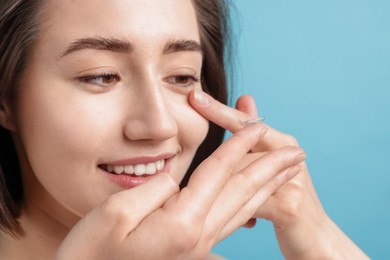 Photo of Woman putting in contact lens on light blue background, closeup