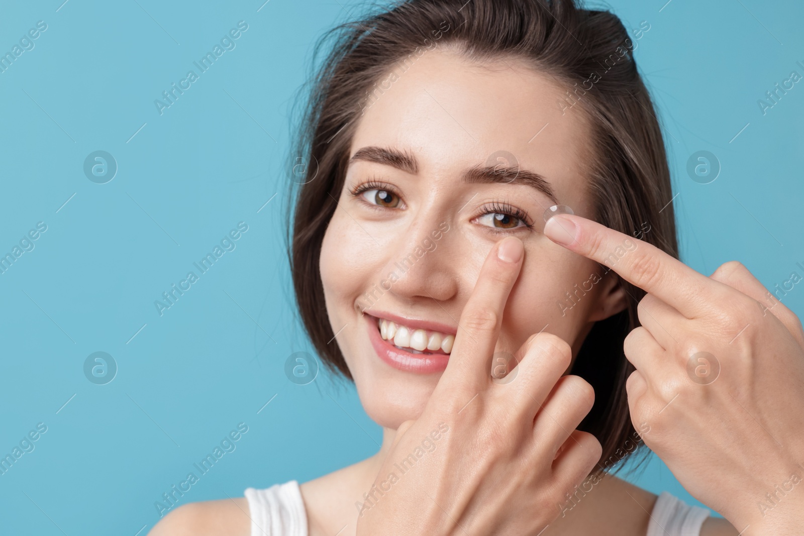 Woman putting in contact lens on light blue background Photo of Woman putting in contact lens on light blue background