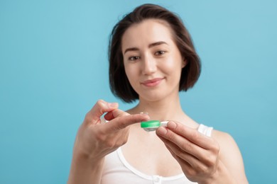 Photo of Woman with contact lens and case on light blue background, selective focus