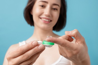 Photo of Woman with contact lens and case on light blue background, selective focus