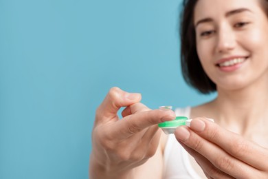 Photo of Woman with contact lens and case on light blue background, selective focus. Space for text