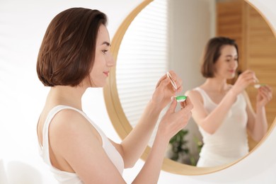 Photo of Woman taking contact lens out of case near mirror indoors