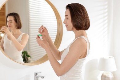 Photo of Woman taking contact lens out of case near mirror indoors