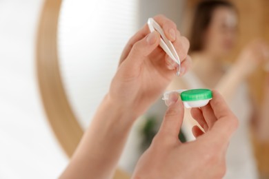 Photo of Woman taking contact lens out of case indoors, closeup