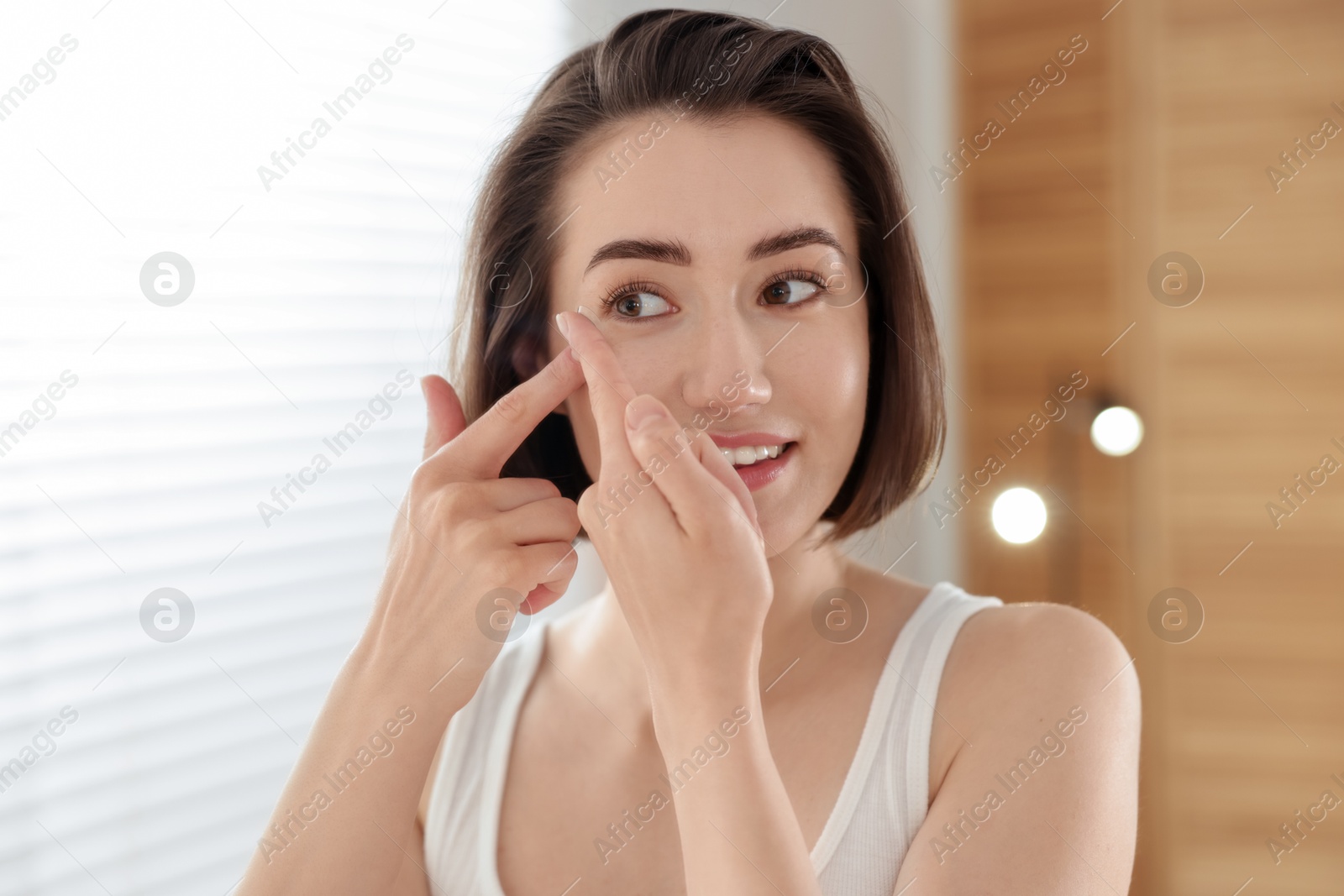 Beautiful woman putting in contact lens indoors Photo of Beautiful woman putting in contact lens indoors
