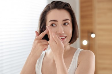 Photo of Beautiful woman putting in contact lens indoors