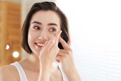Photo of Beautiful woman putting in contact lens indoors. Space for text