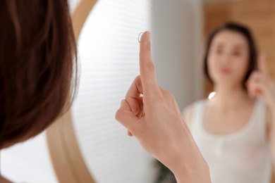 Photo of Woman with contact lens near mirror indoors, selective focus