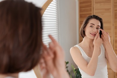 Photo of Woman putting in contact lens near mirror indoors
