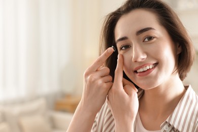 Photo of Beautiful woman putting in contact lens indoors. Space for text