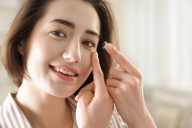Photo of Beautiful woman putting in contact lens indoors