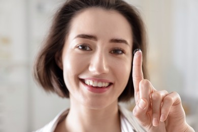 Photo of Happy woman with contact lens on her finger indoors