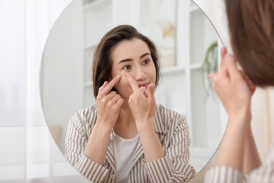 Photo of Woman putting in contact lens near mirror indoors