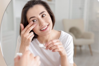 Photo of Woman putting in contact lens near mirror indoors