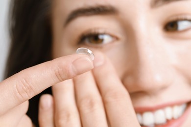 Photo of Woman putting in contact lens on light background, closeup